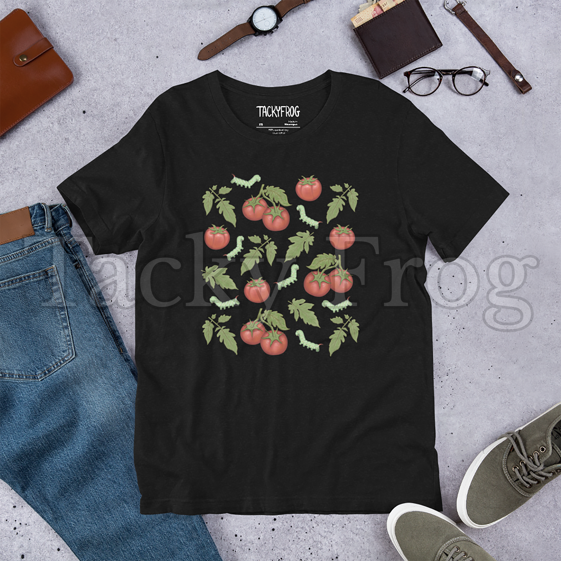 A mockup of an black heather-colored tomato hornworm caterpillar t-shirt amongst some clutter.